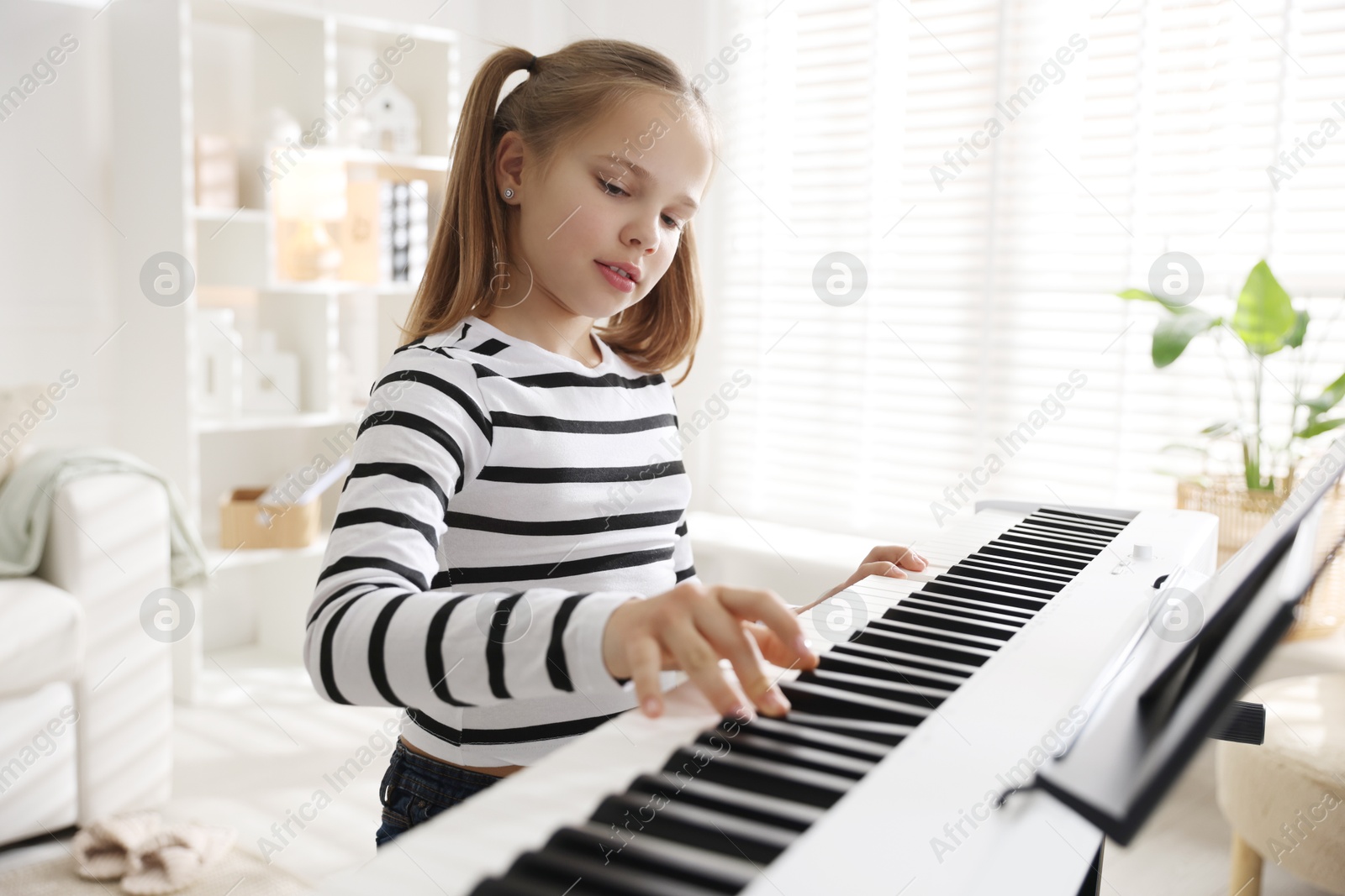 Photo of Cute girl playing synthesizer at home. Electronic musical instrument