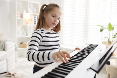 Photo of Cute girl playing synthesizer at home. Electronic musical instrument