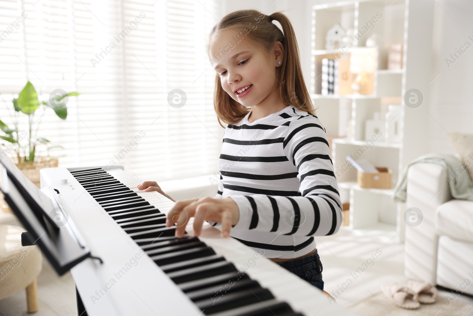 Photo of Cute girl playing synthesizer at home. Electronic musical instrument