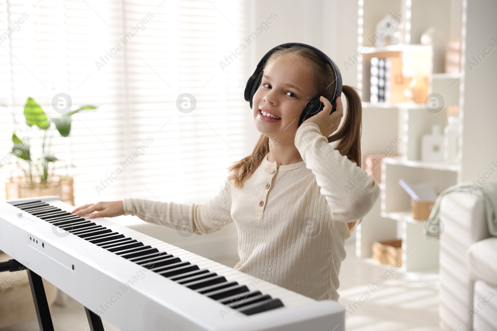 Photo of Cute girl in headphones playing synthesizer at home