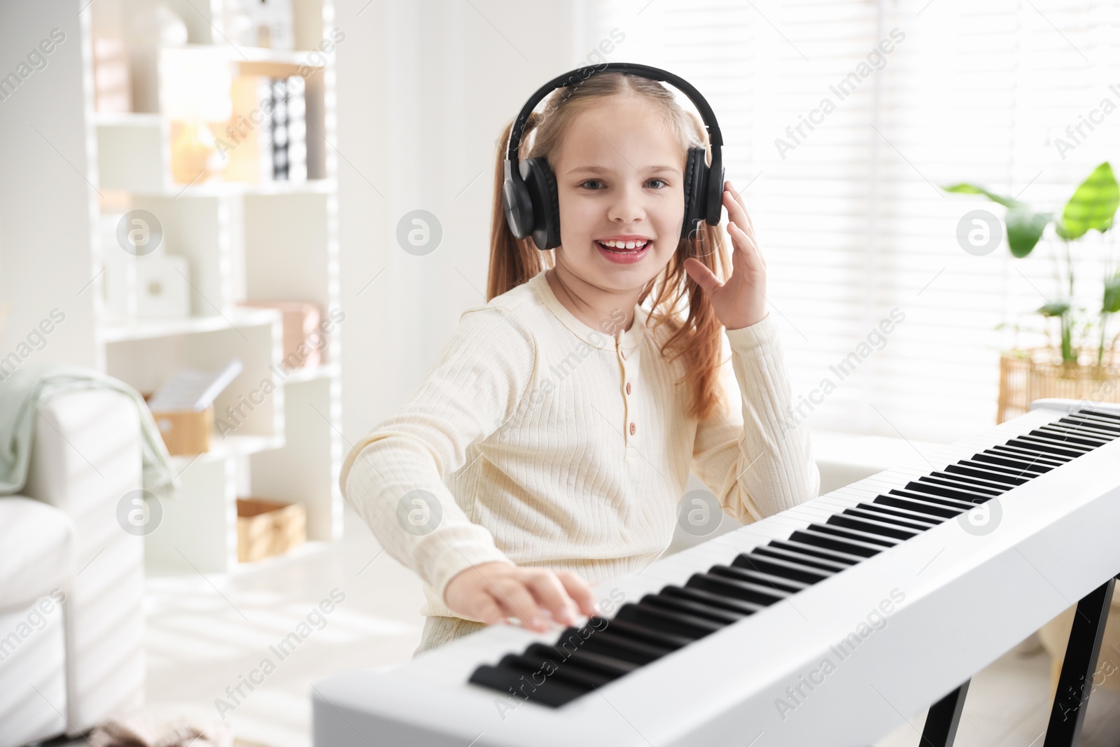 Photo of Cute girl in headphones playing synthesizer at home