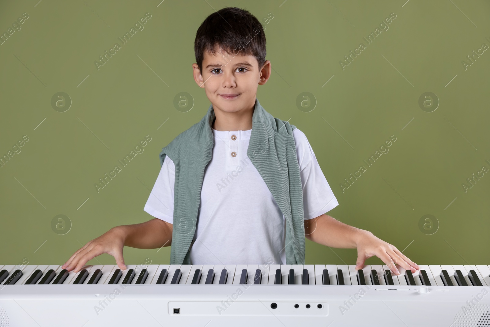 Photo of Cute boy playing synthesizer on olive background