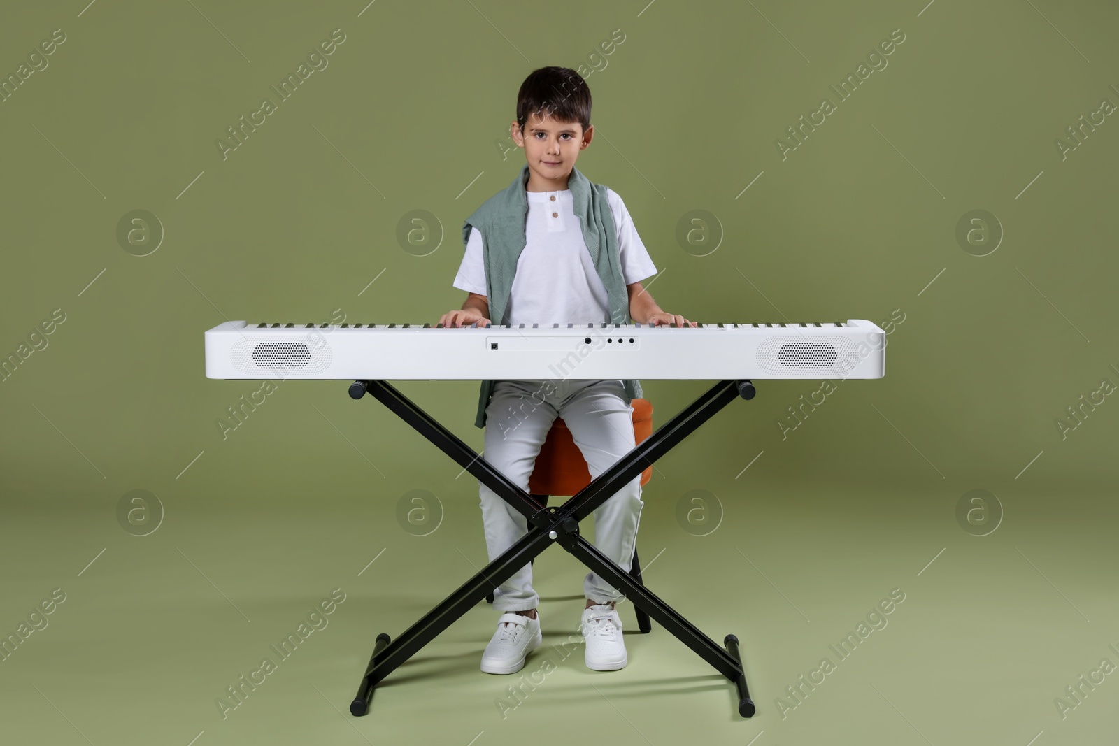 Photo of Cute boy playing synthesizer on olive background