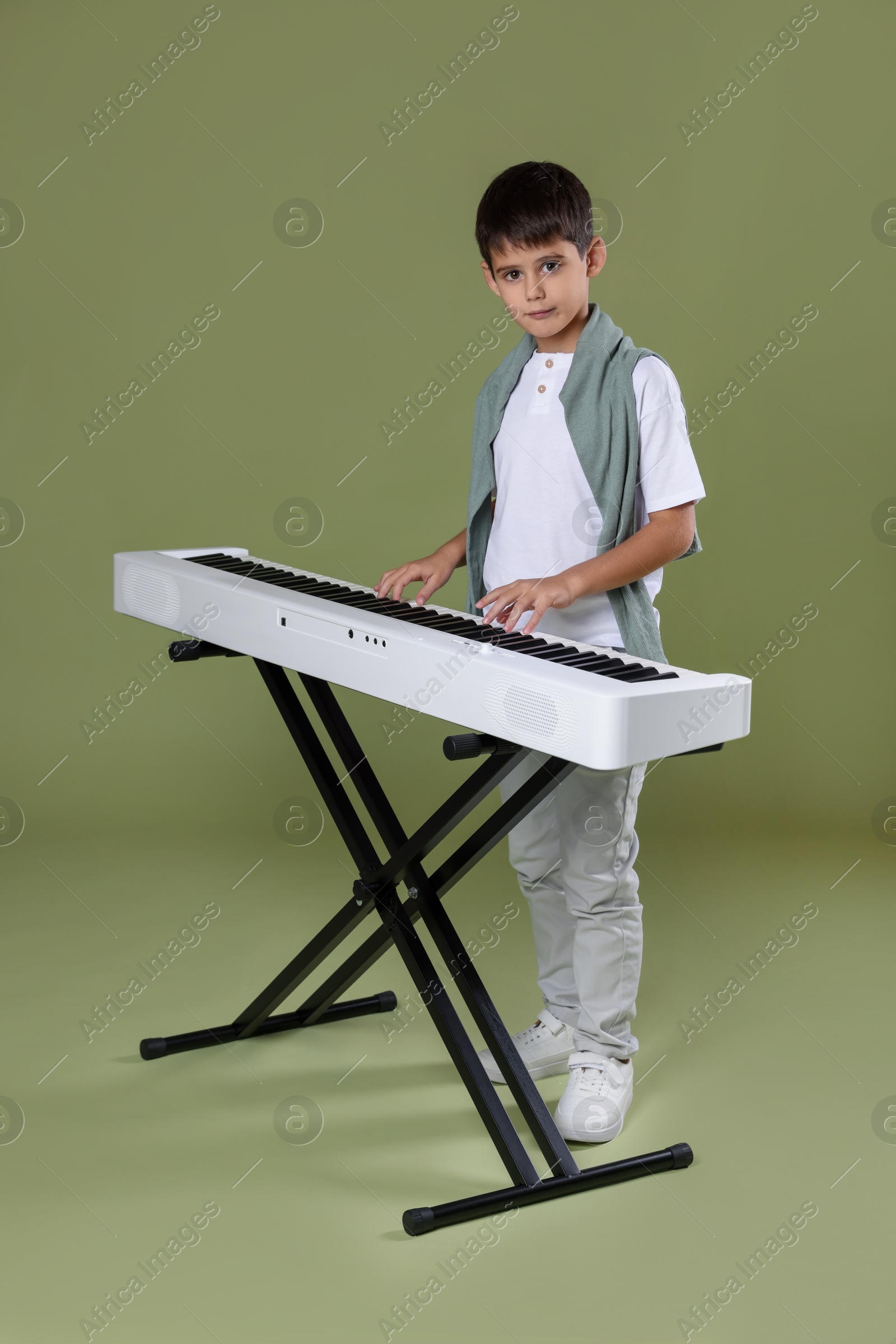 Photo of Cute boy playing synthesizer on olive background