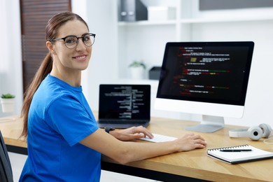 Photo of Programmer working on laptop and computer at wooden desk indoors