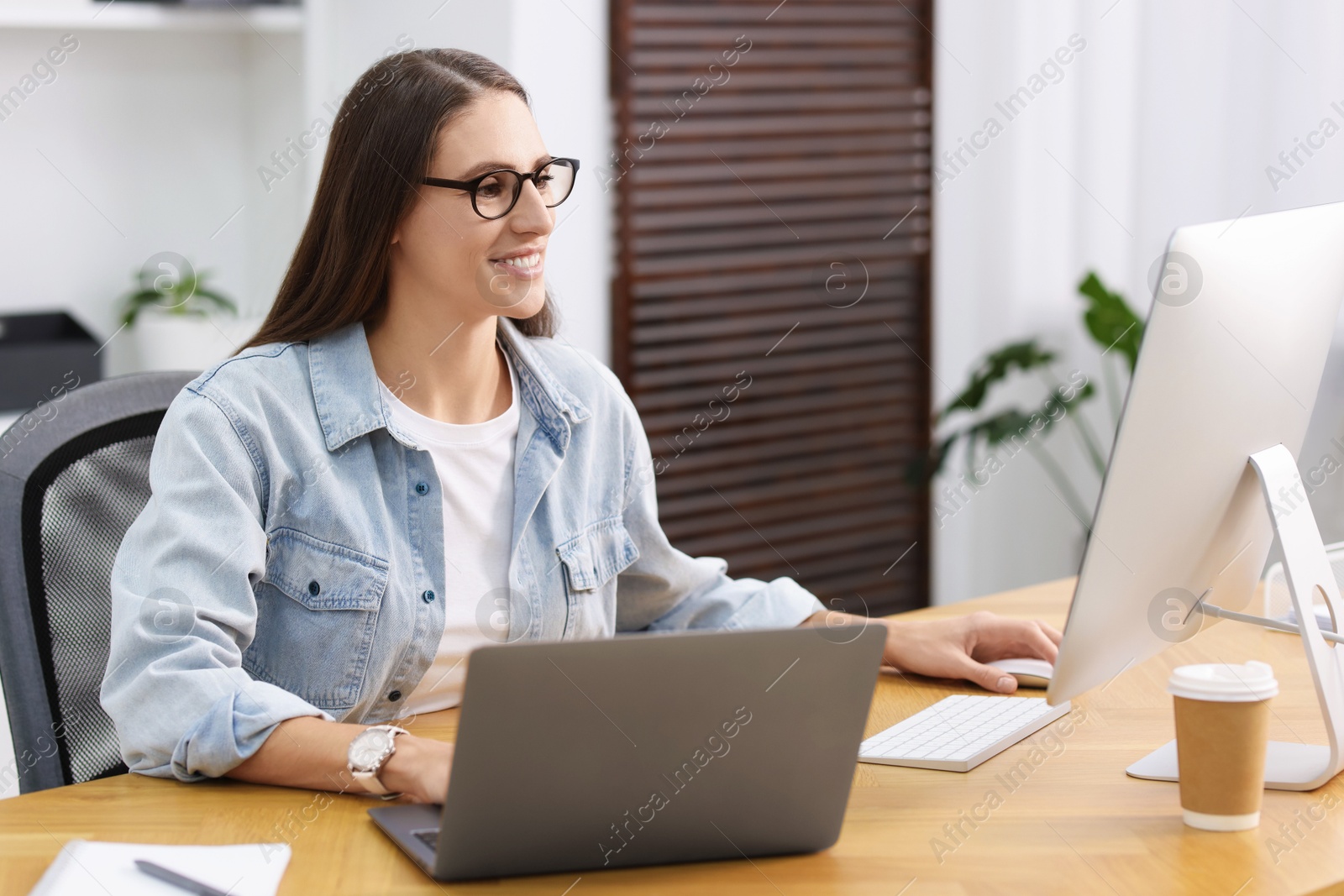 Photo of Programmer working on laptop and computer at wooden desk indoors