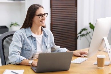 Photo of Programmer working on laptop and computer at wooden desk indoors