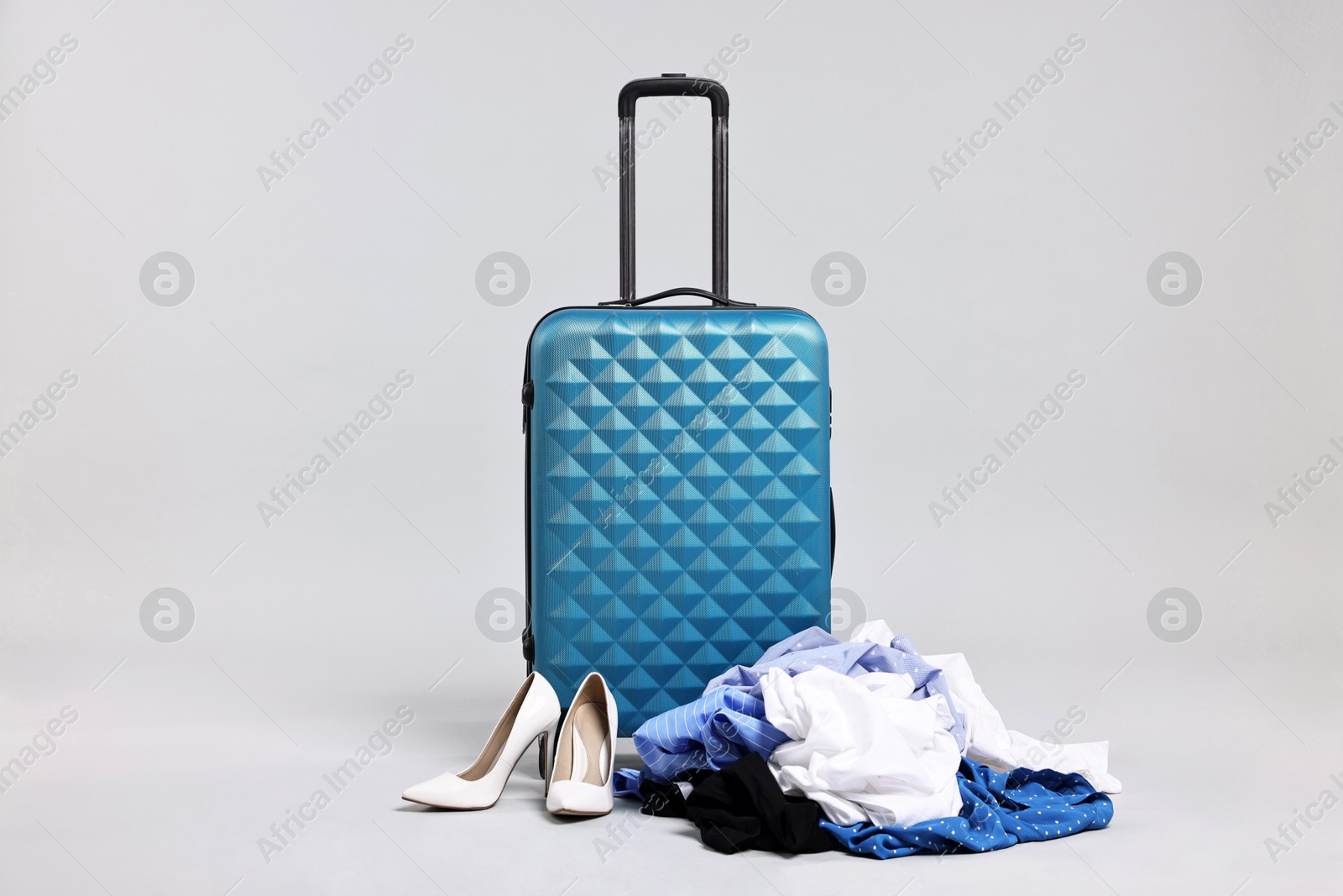 Photo of Suitcase and messy pile of clothes on grey background