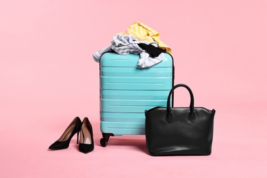 Photo of Suitcase, messy clothes, bag and shoes on pink background