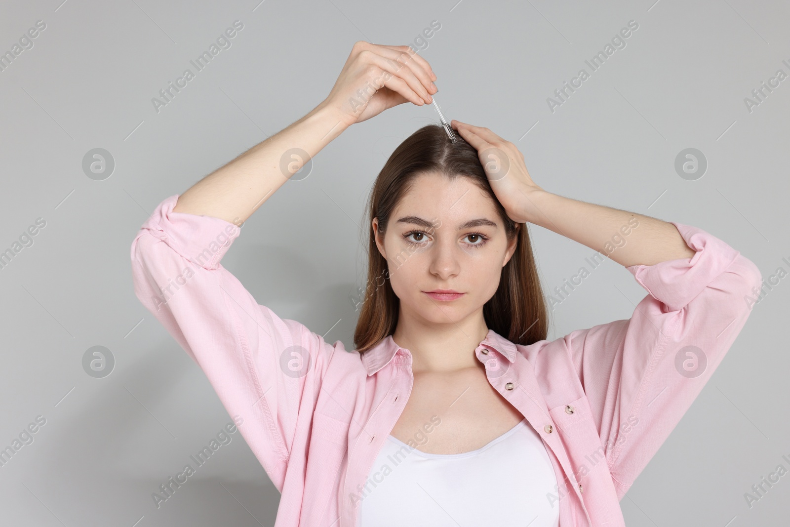 Photo of Hair loss problem. Girl applying serum onto hairline on grey background