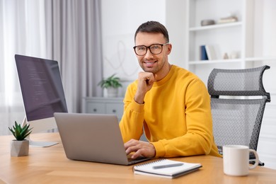 Photo of Programmer with laptop at wooden desk indoors