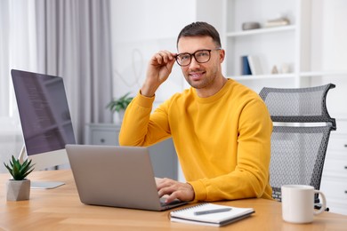 Photo of Programmer with laptop at wooden desk indoors