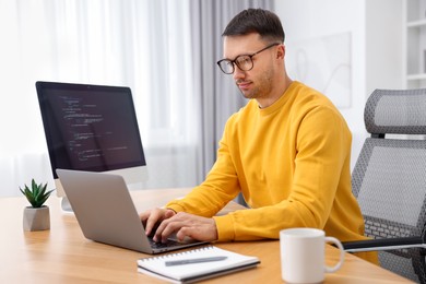 Photo of Programmer working on laptop at wooden desk indoors