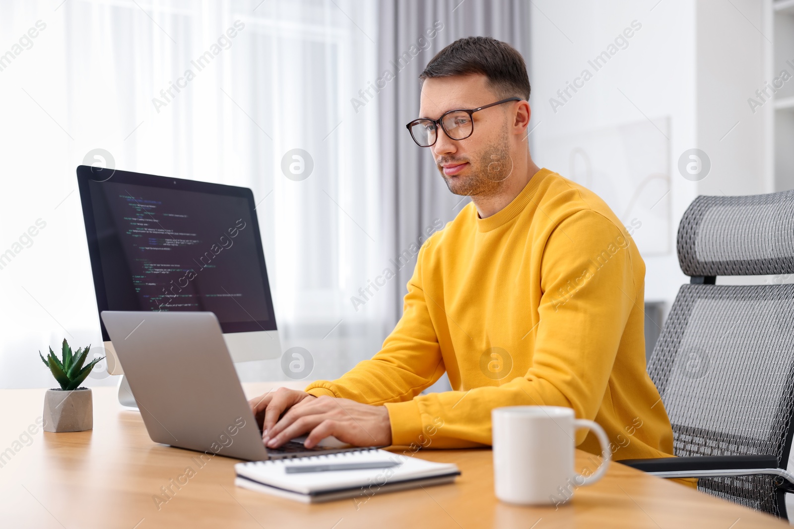 Photo of Programmer working on laptop at wooden desk indoors