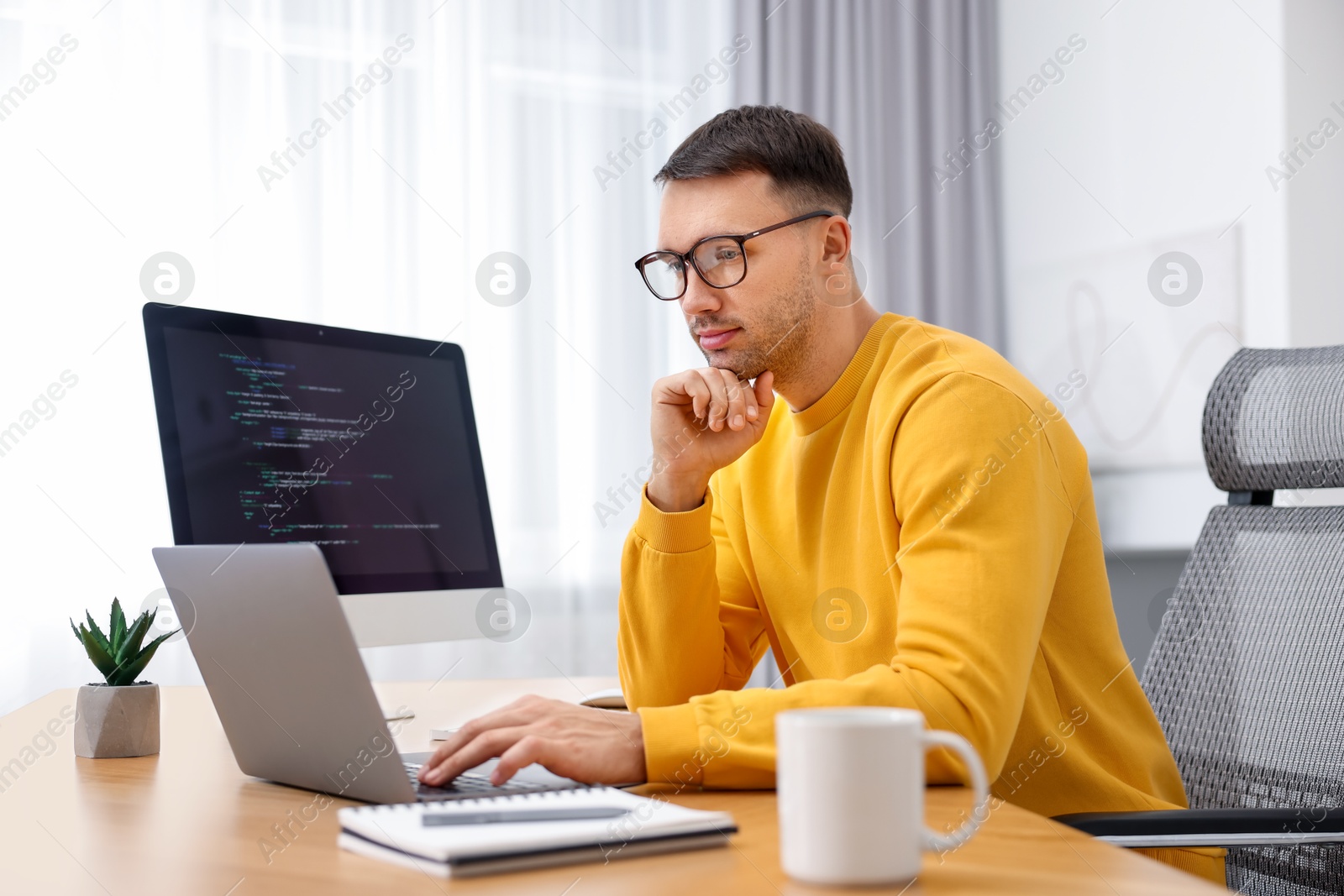 Photo of Programmer working on laptop at wooden desk indoors