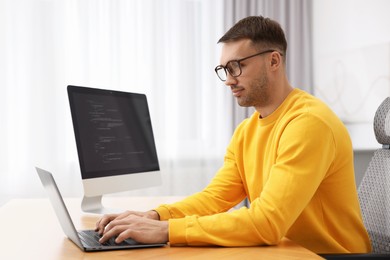 Photo of Programmer working on laptop at wooden desk indoors