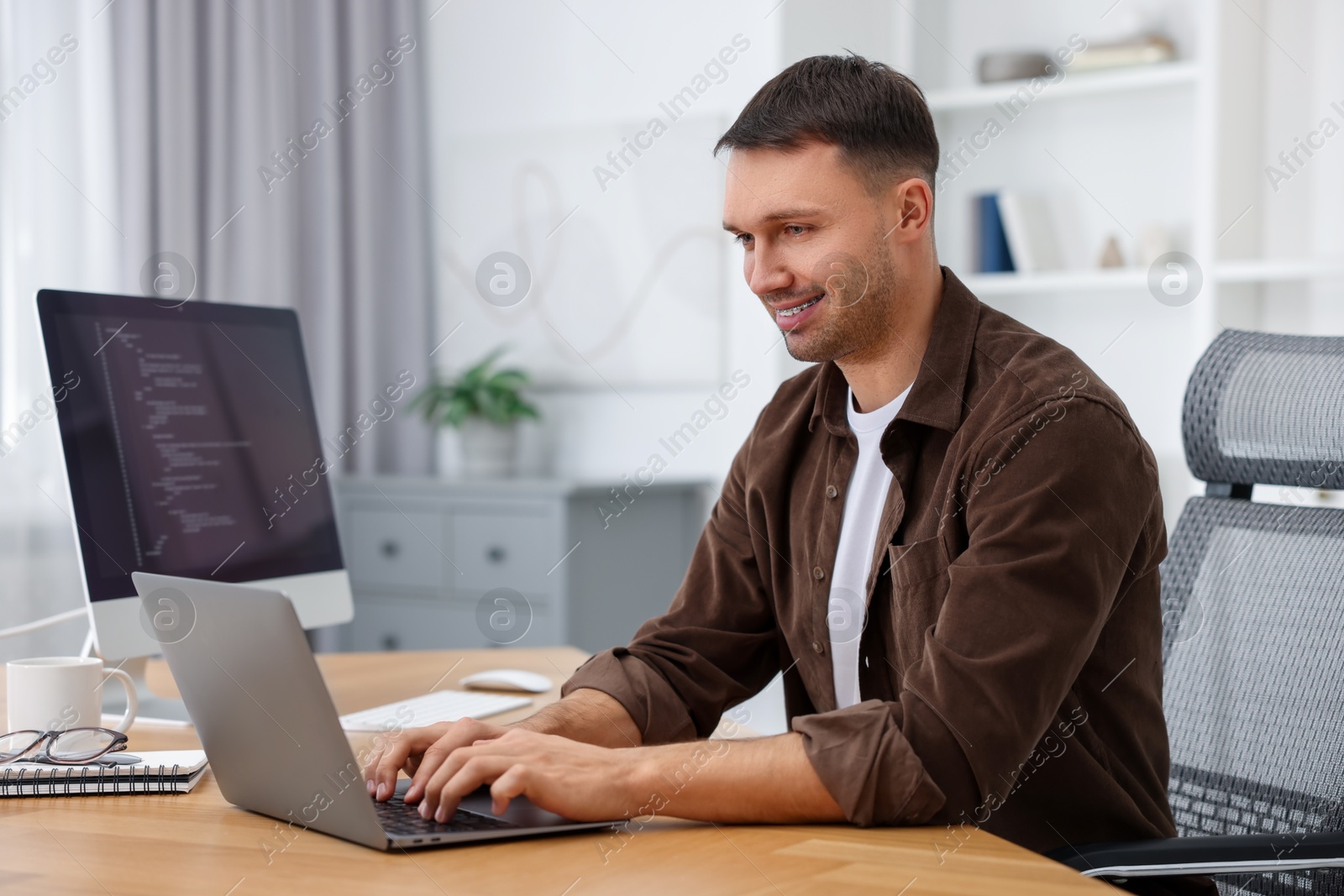 Photo of Programmer working on laptop at wooden desk indoors