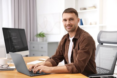 Photo of Programmer with laptop at wooden desk indoors