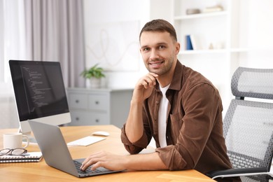 Photo of Programmer with laptop at wooden desk indoors