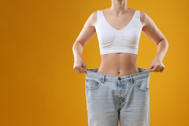 Photo of Weight loss. Woman wearing big jeans on yellow background, closeup. Space for text