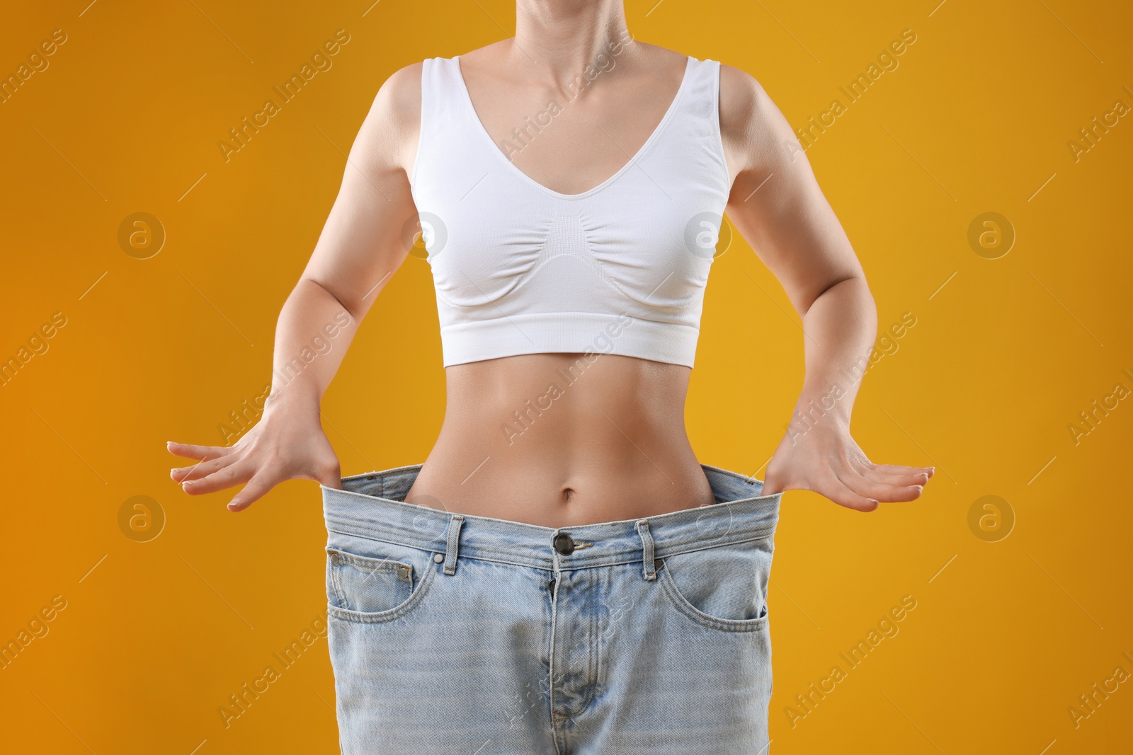 Photo of Weight loss. Woman wearing big jeans on yellow background, closeup