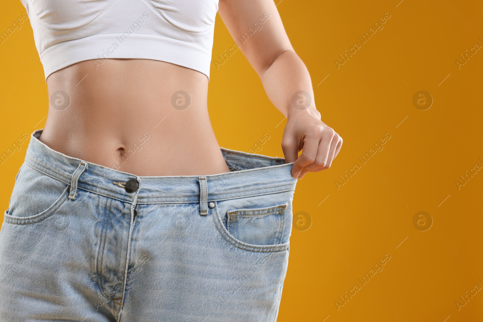 Photo of Weight loss. Woman wearing big jeans on yellow background, closeup. Space for text