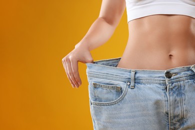 Photo of Weight loss. Woman wearing big jeans on yellow background, closeup. Space for text