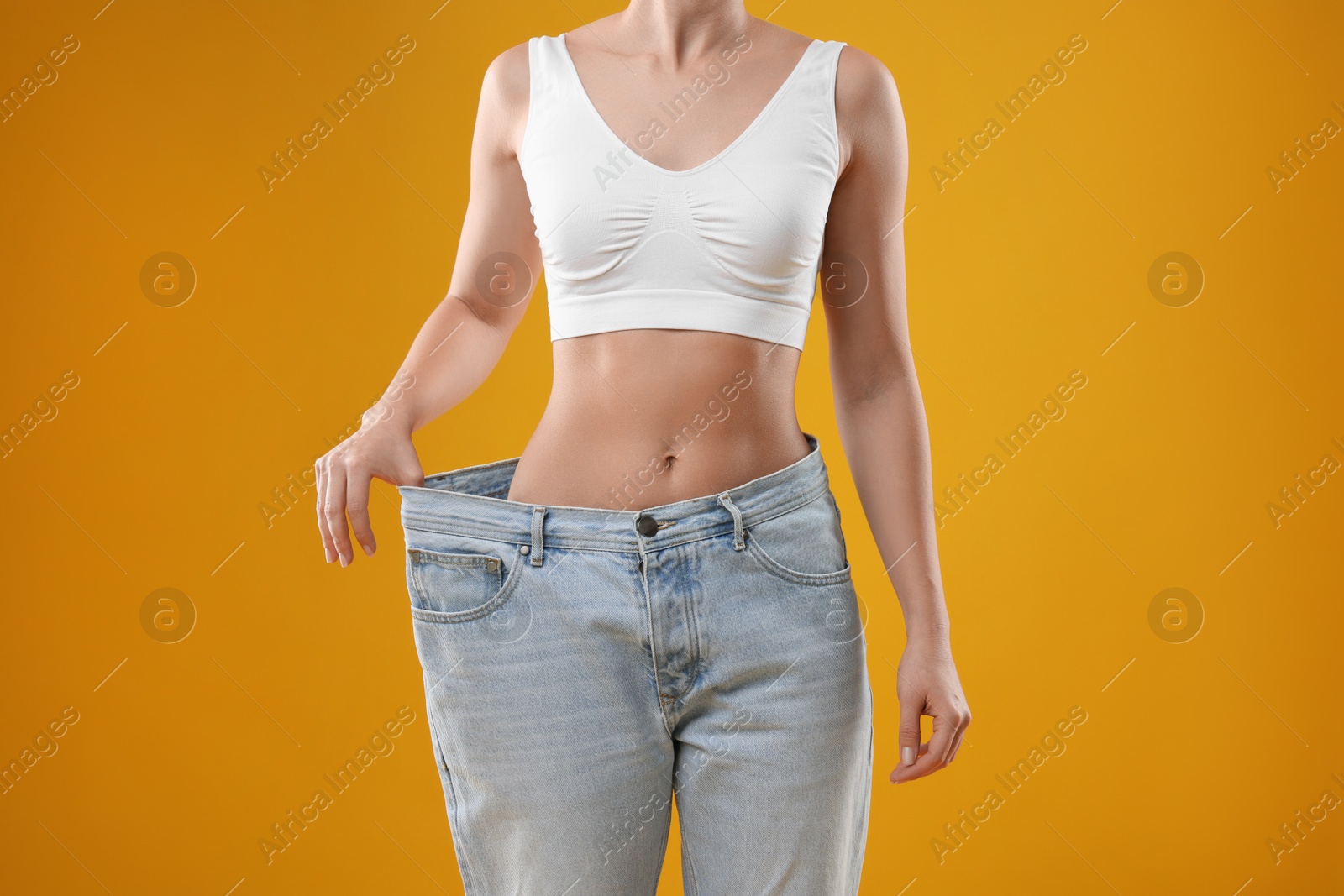 Photo of Weight loss. Woman wearing big jeans on yellow background, closeup