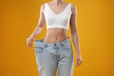 Photo of Weight loss. Woman wearing big jeans on yellow background, closeup