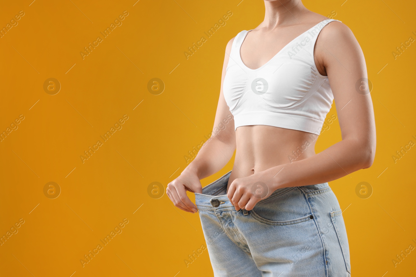 Photo of Weight loss. Woman wearing big jeans on yellow background, closeup. Space for text