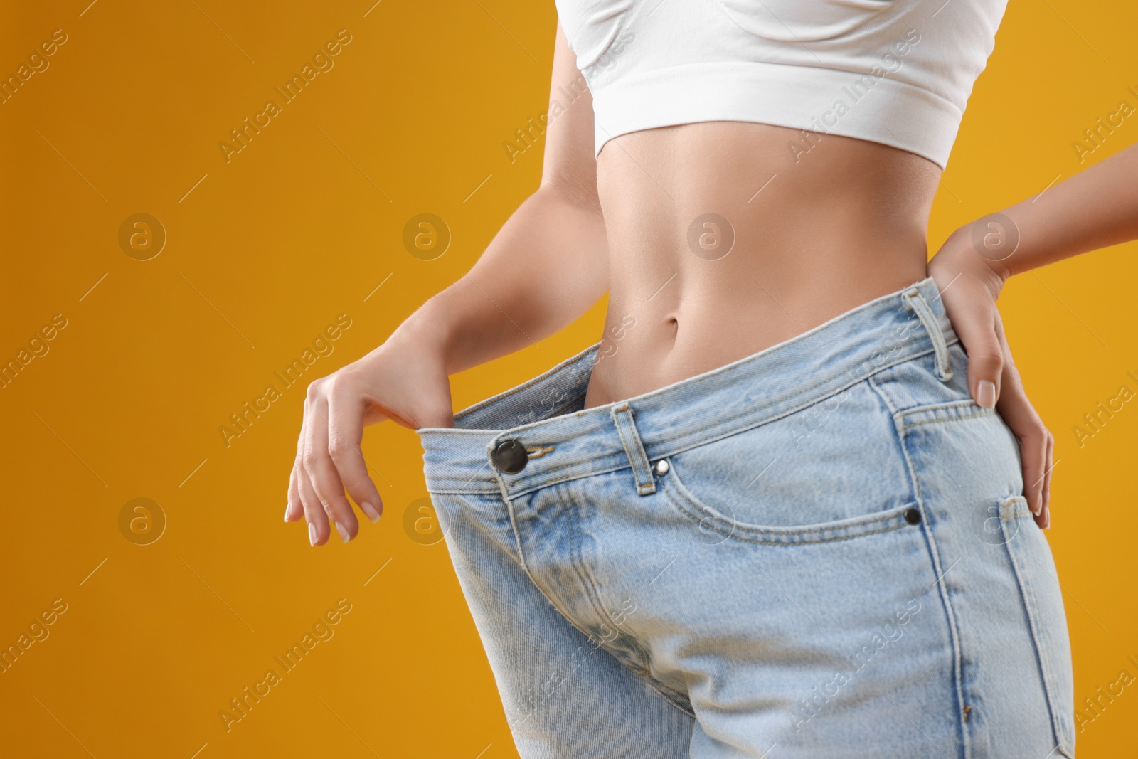 Photo of Weight loss. Woman wearing big jeans on yellow background, closeup