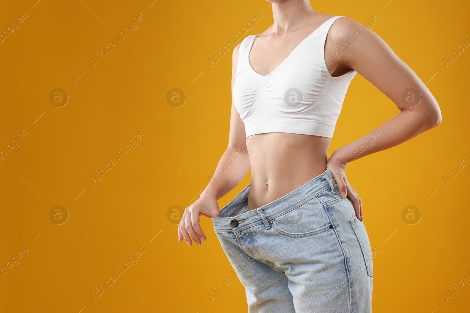 Photo of Weight loss. Woman wearing big jeans on yellow background, closeup. Space for text