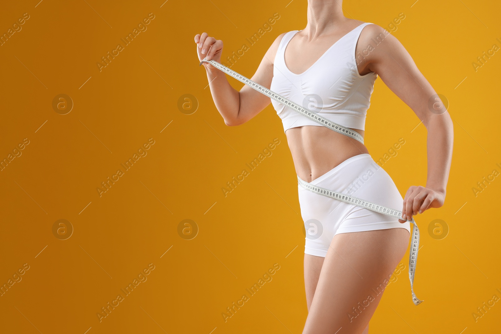 Photo of Weight loss. Woman measuring her slim waist with tape on yellow background, closeup. Space for text