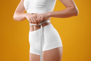 Photo of Weight loss. Woman measuring her slim waist with tape on yellow background, closeup