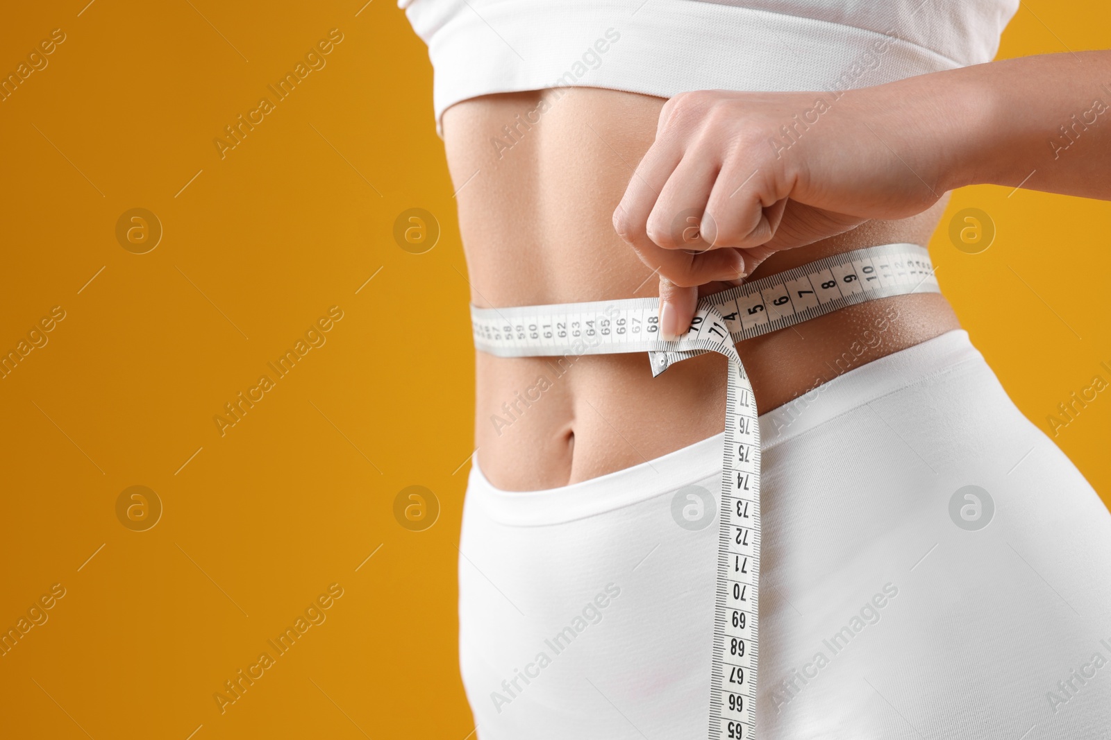 Photo of Weight loss. Woman measuring her slim waist with tape on yellow background, closeup. Space for text