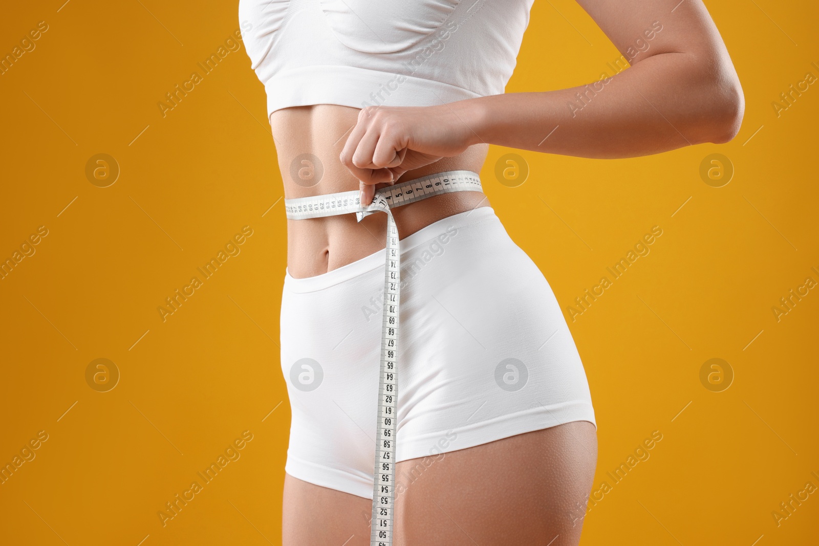 Photo of Weight loss. Woman measuring her slim waist with tape on yellow background, closeup