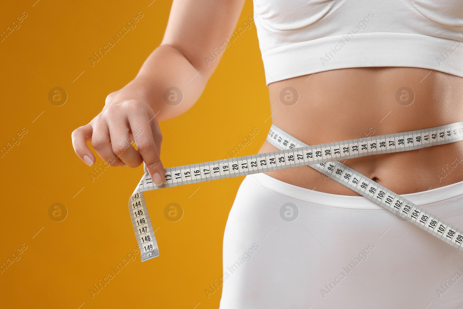 Photo of Weight loss. Woman measuring her slim waist with tape on yellow background, closeup