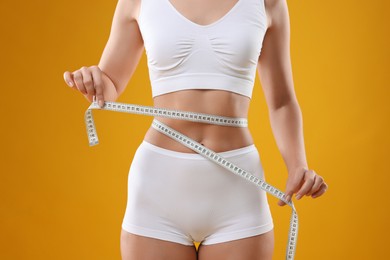 Photo of Weight loss. Woman measuring her slim waist with tape on yellow background, closeup