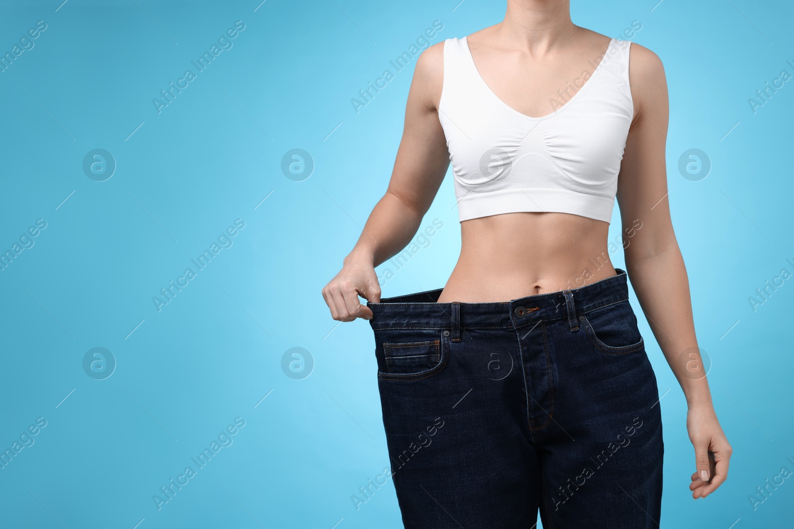 Photo of Weight loss. Woman wearing big jeans on light blue background, closeup. Space for text