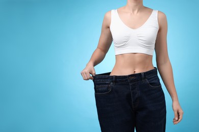 Photo of Weight loss. Woman wearing big jeans on light blue background, closeup. Space for text