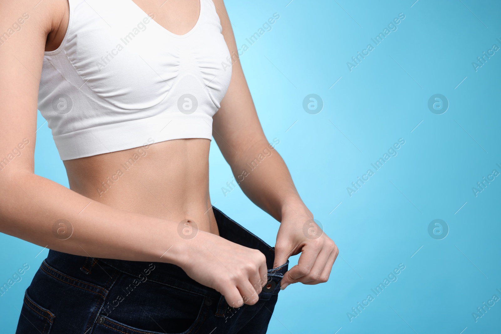 Photo of Weight loss. Woman wearing big jeans on light blue background, closeup. Space for text