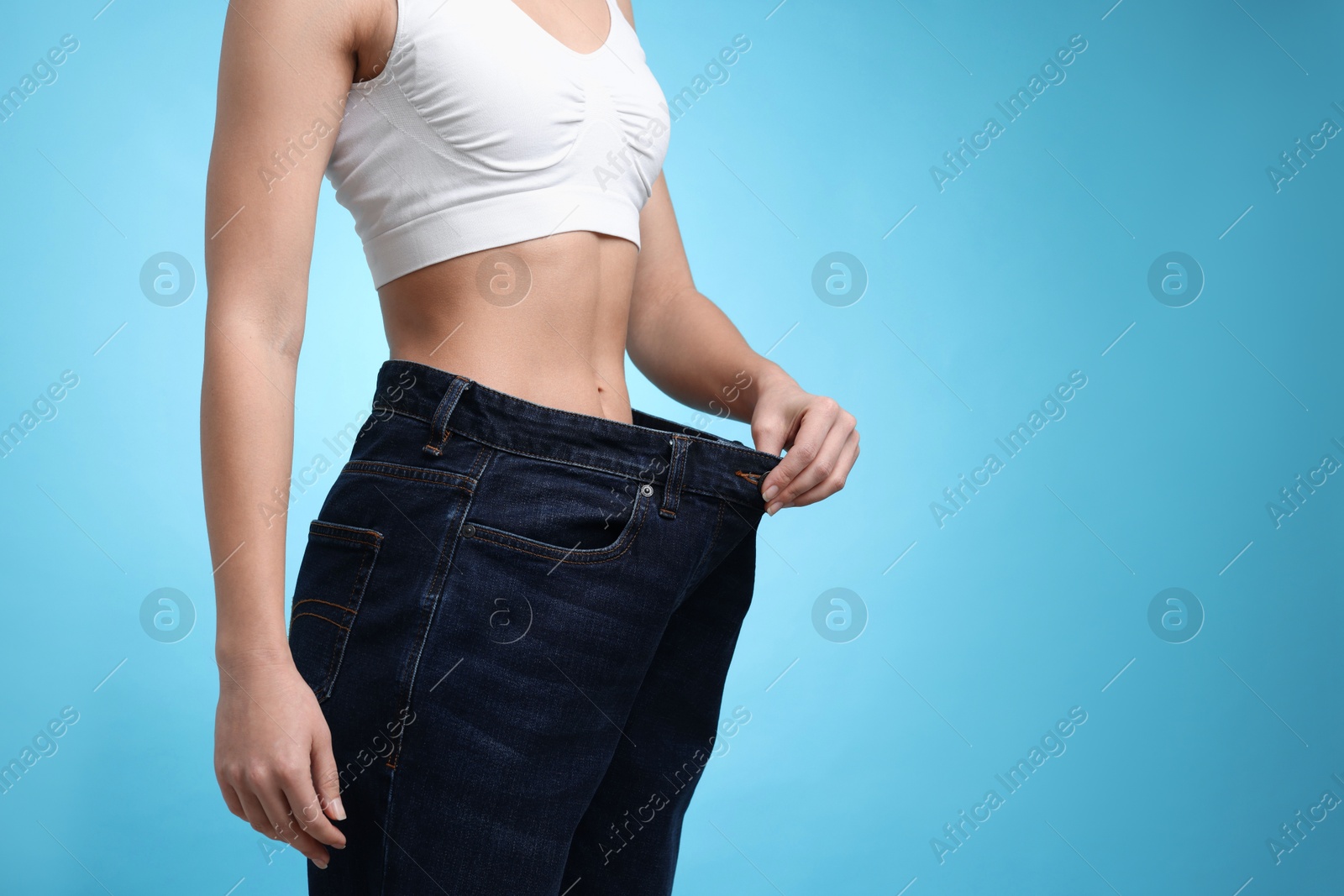 Photo of Weight loss. Woman wearing big jeans on light blue background, closeup. Space for text