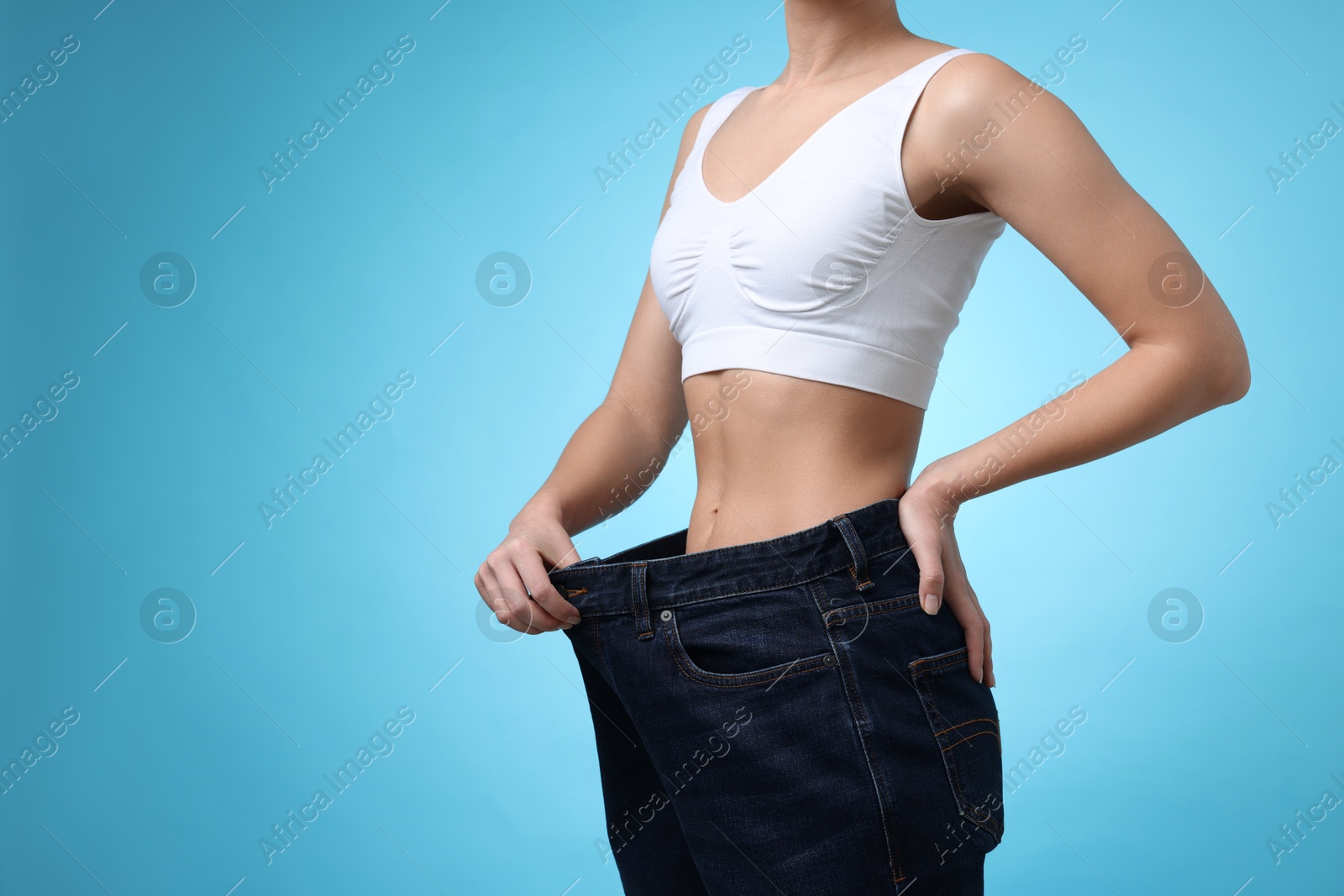 Photo of Weight loss. Woman wearing big jeans on light blue background, closeup. Space for text