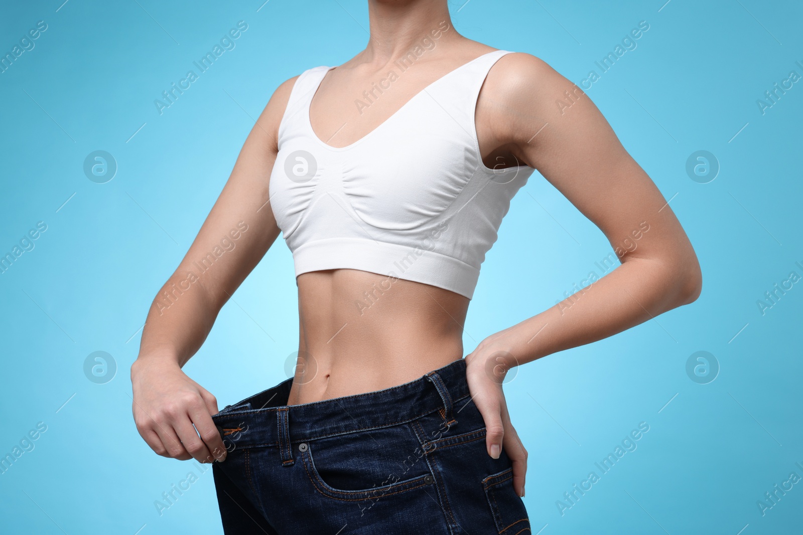 Photo of Weight loss. Woman wearing big jeans on light blue background, closeup