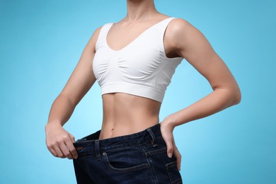 Photo of Weight loss. Woman wearing big jeans on light blue background, closeup