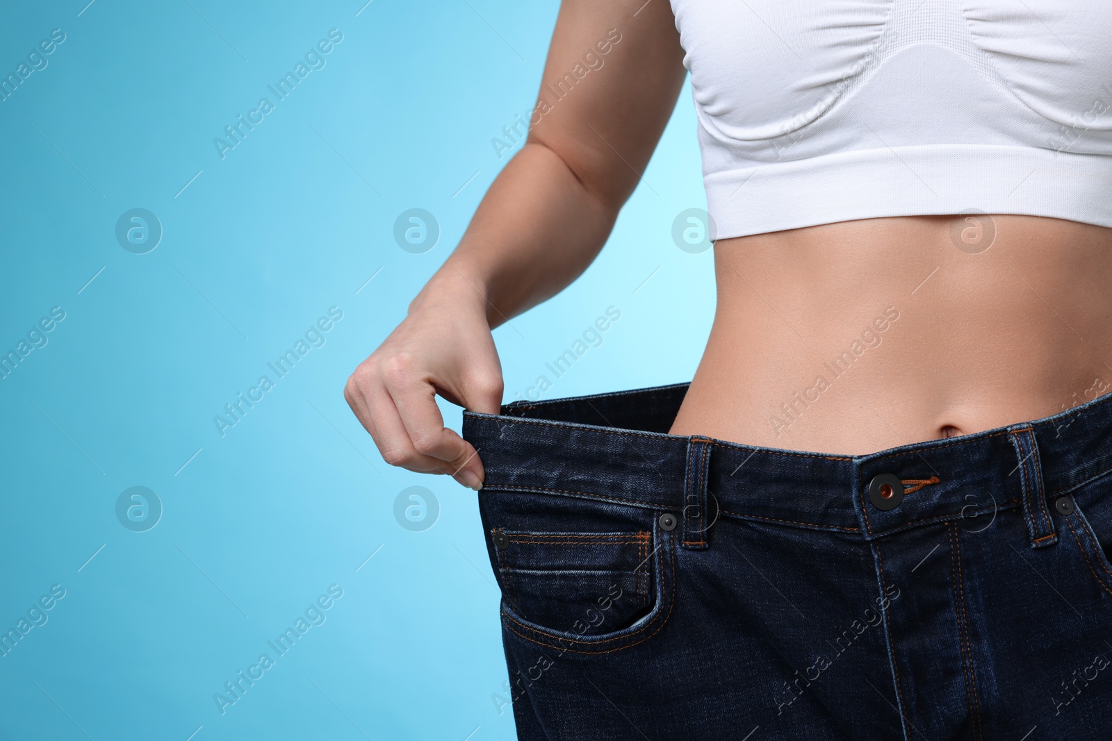 Photo of Weight loss. Woman wearing big jeans on light blue background, closeup. Space for text