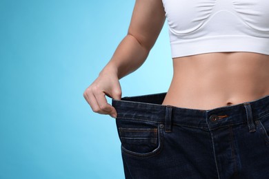 Photo of Weight loss. Woman wearing big jeans on light blue background, closeup. Space for text