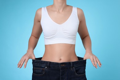 Photo of Weight loss. Woman wearing big jeans on light blue background, closeup