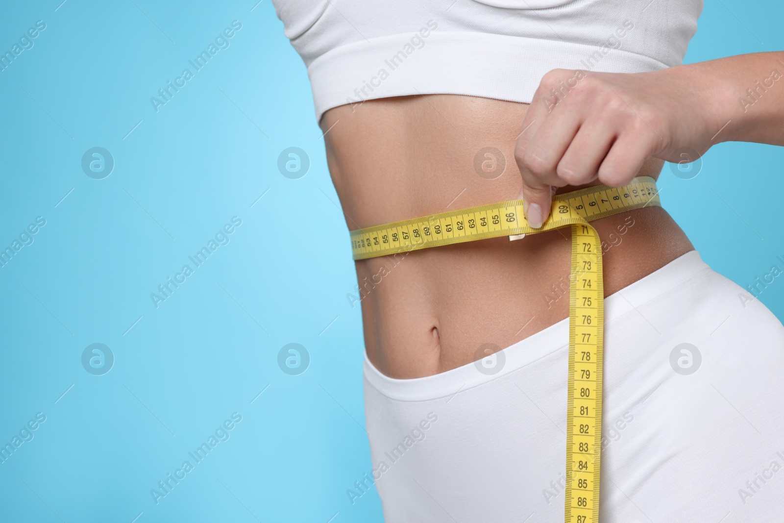 Photo of Weight loss. Woman measuring her slim waist with tape on light blue background, closeup. Space for text