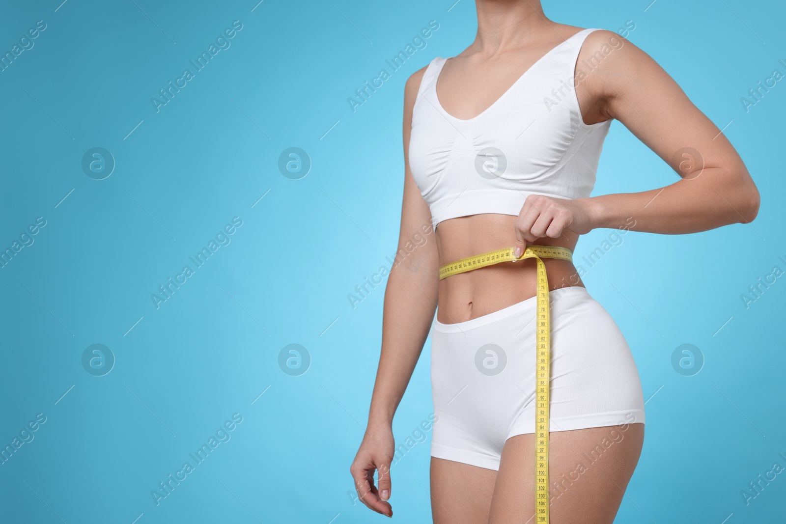 Photo of Weight loss. Woman measuring her slim waist with tape on light blue background, closeup. Space for text